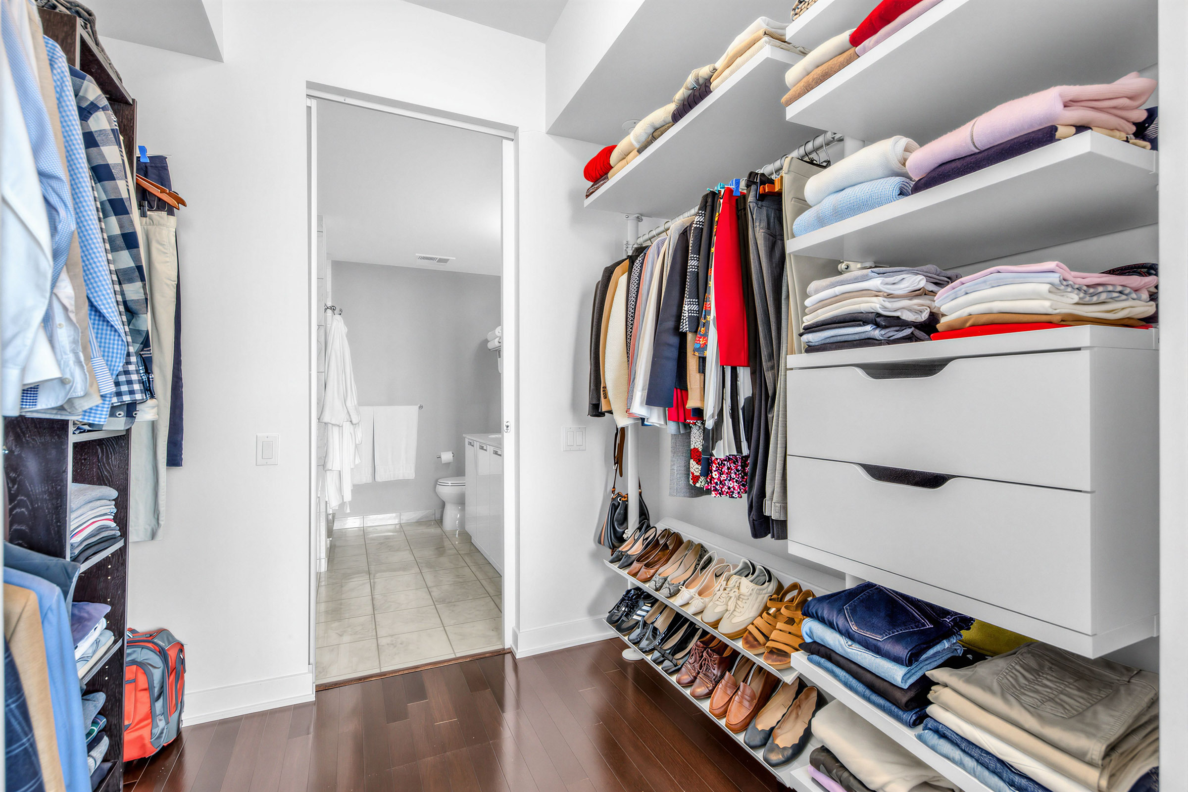 Large his and her closets with clothes hanging from rods and compartments, and shoes on shelves.