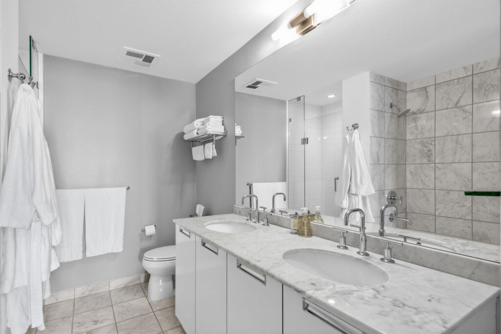 33 Charles St E Unit 3206 5-piece ensuite bath with his and her sinks, cabinets, ceramic floors, toilet and wall-mounted towel rack.