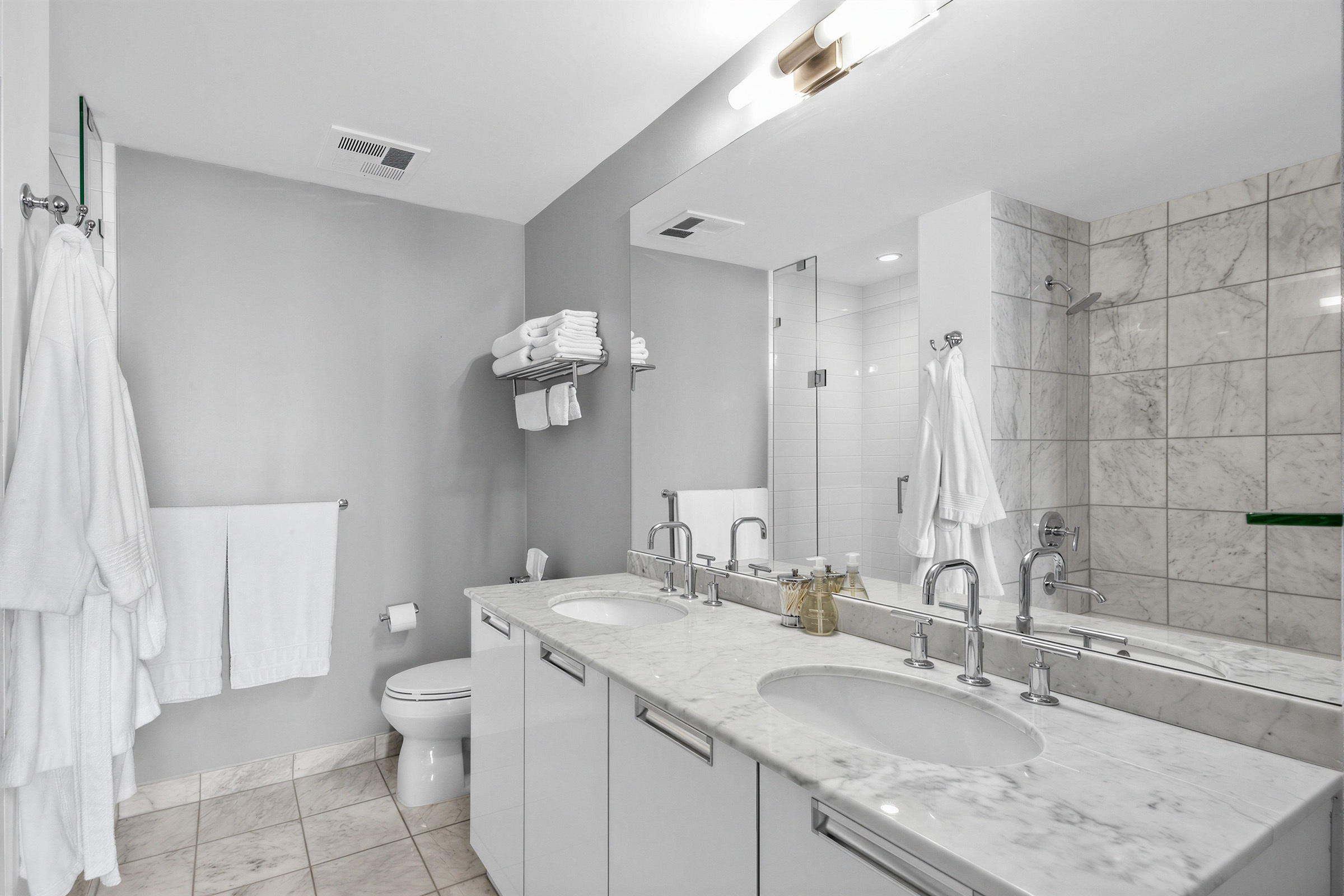 33 Charles St E Unit 3206 5-piece ensuite bath with his and her sinks, cabinets, ceramic floors, toilet and wall-mounted towel rack.