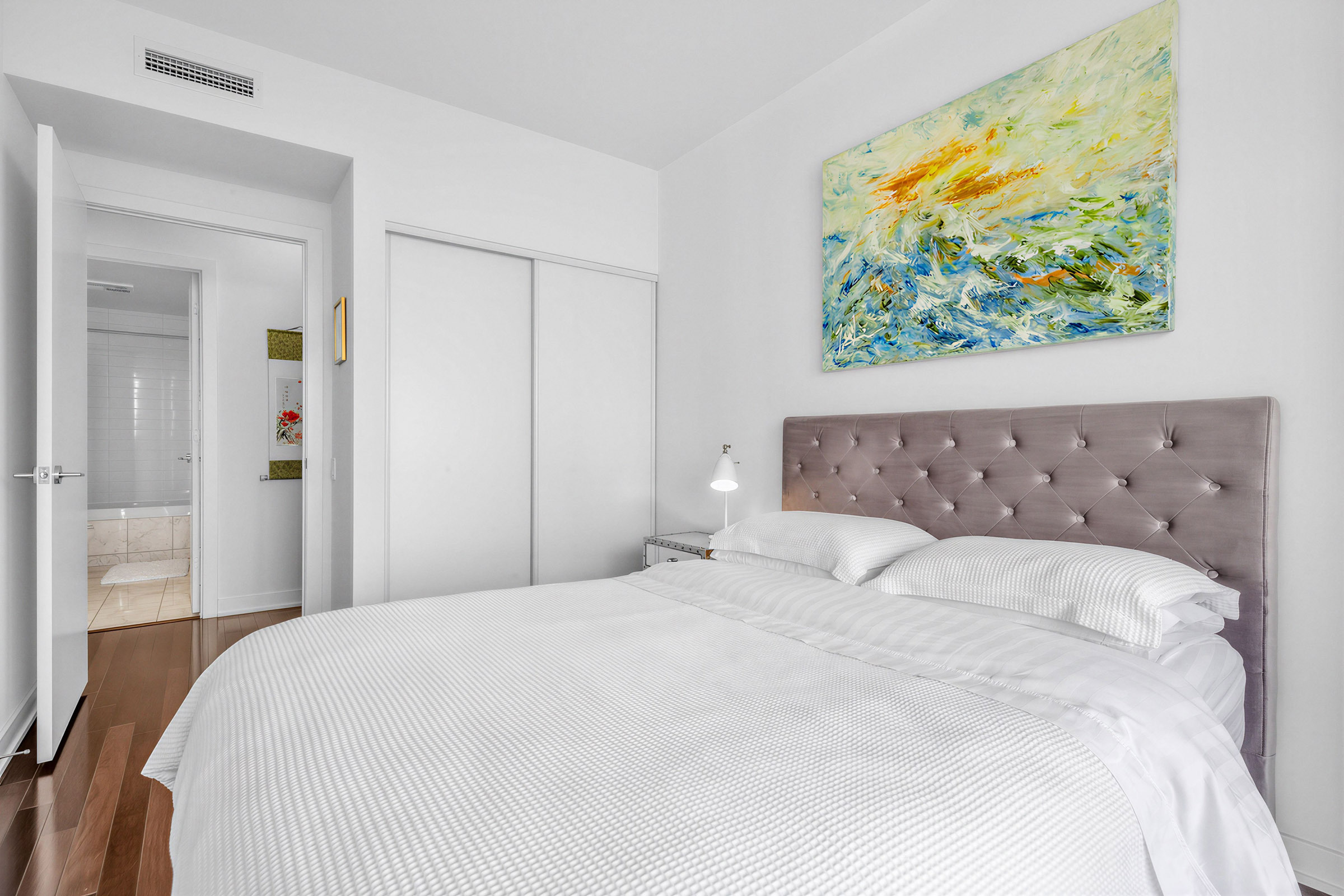 Condo bedroom with large close, bed, hardwood floors and view of bathroom.