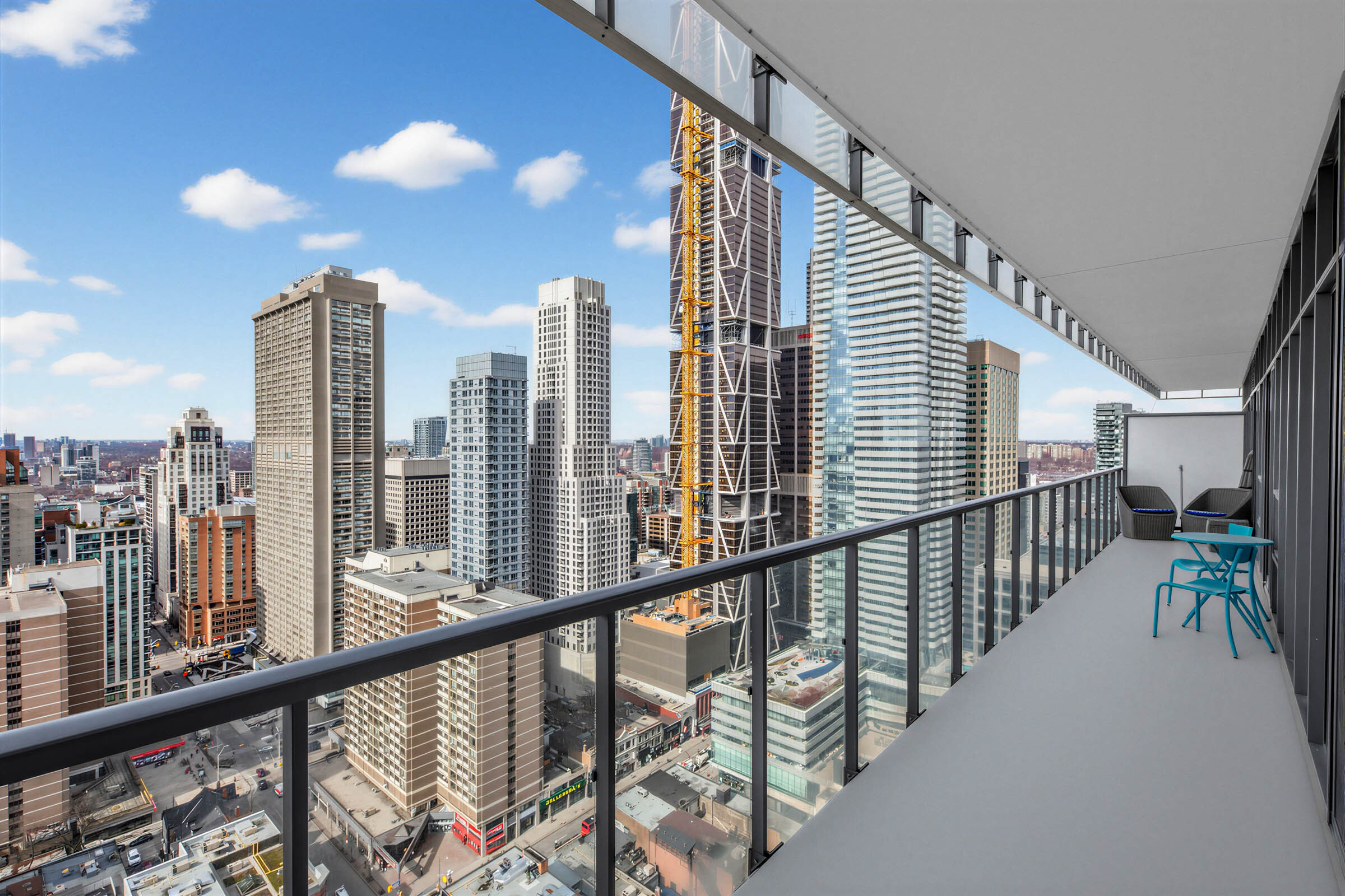 33 Charles St E Unit 3206 long balcony with blue chairs, table, and clear glass panels showing Toronto skyline.