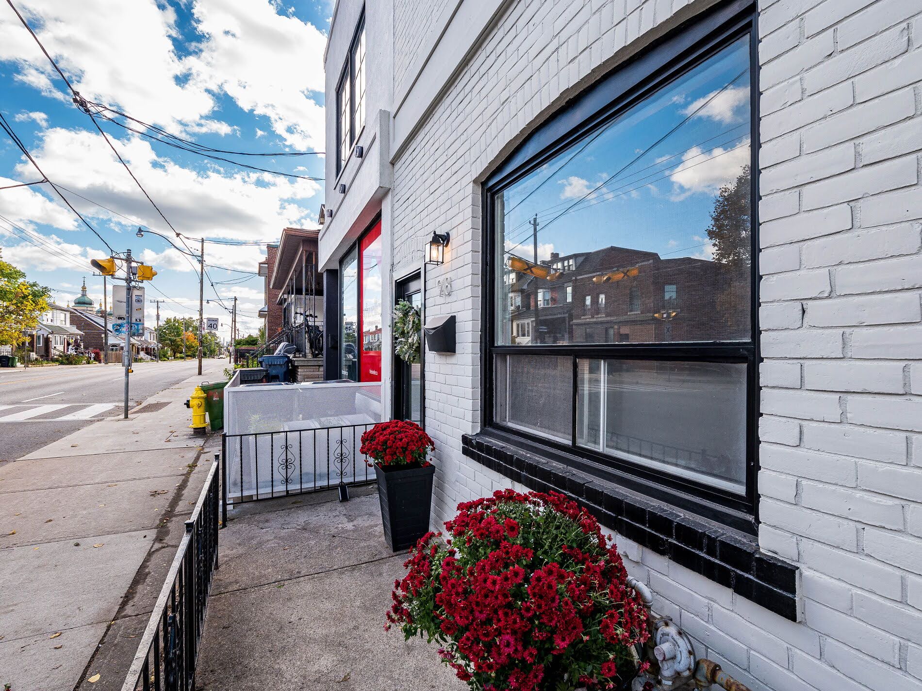 View of Ossington Ave sidewalk, empty streets, low-rise buildings and skies.