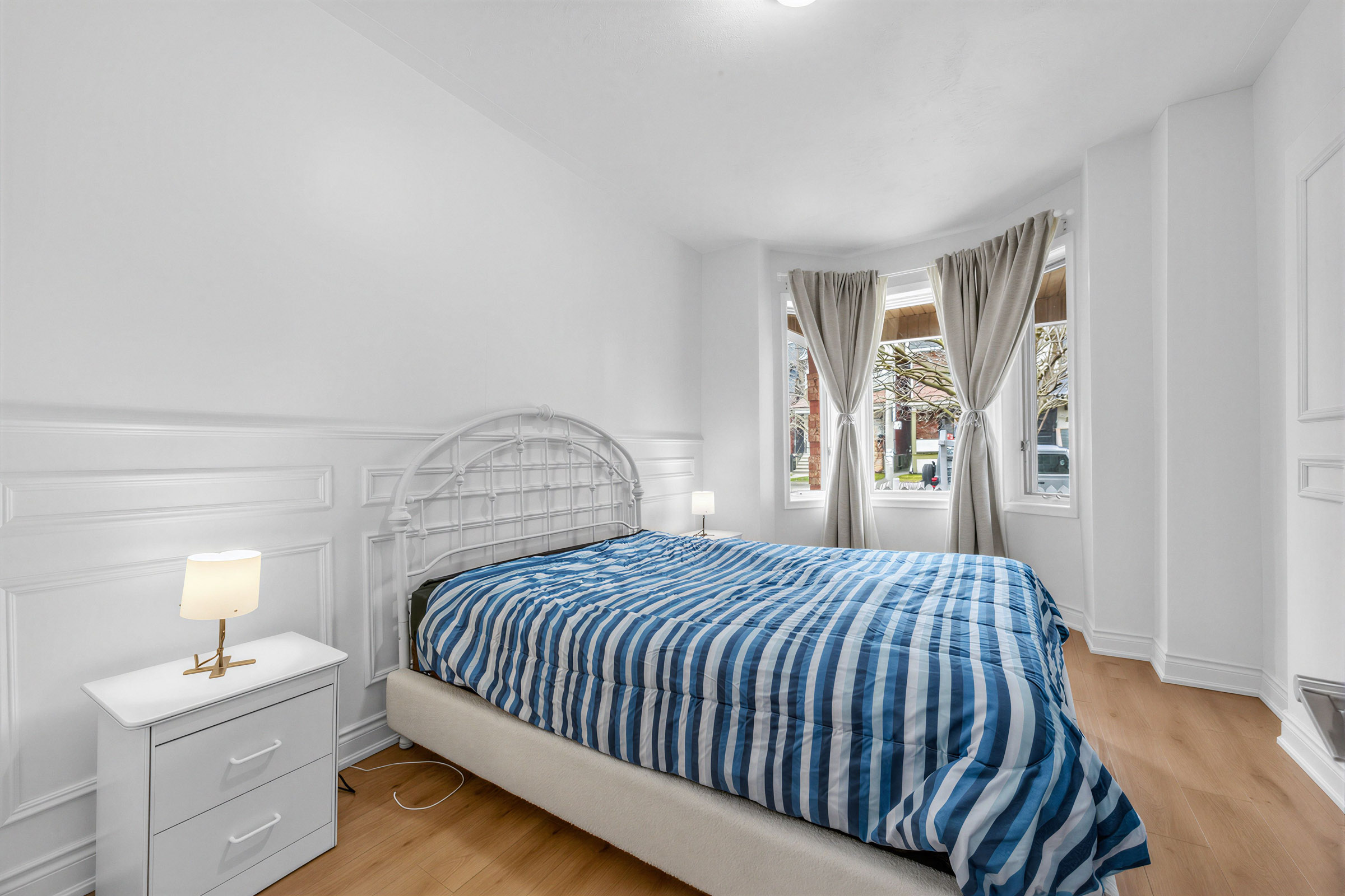 57 Shanly St large primary bedroom with large bed and 3-panel bay window with view of street.