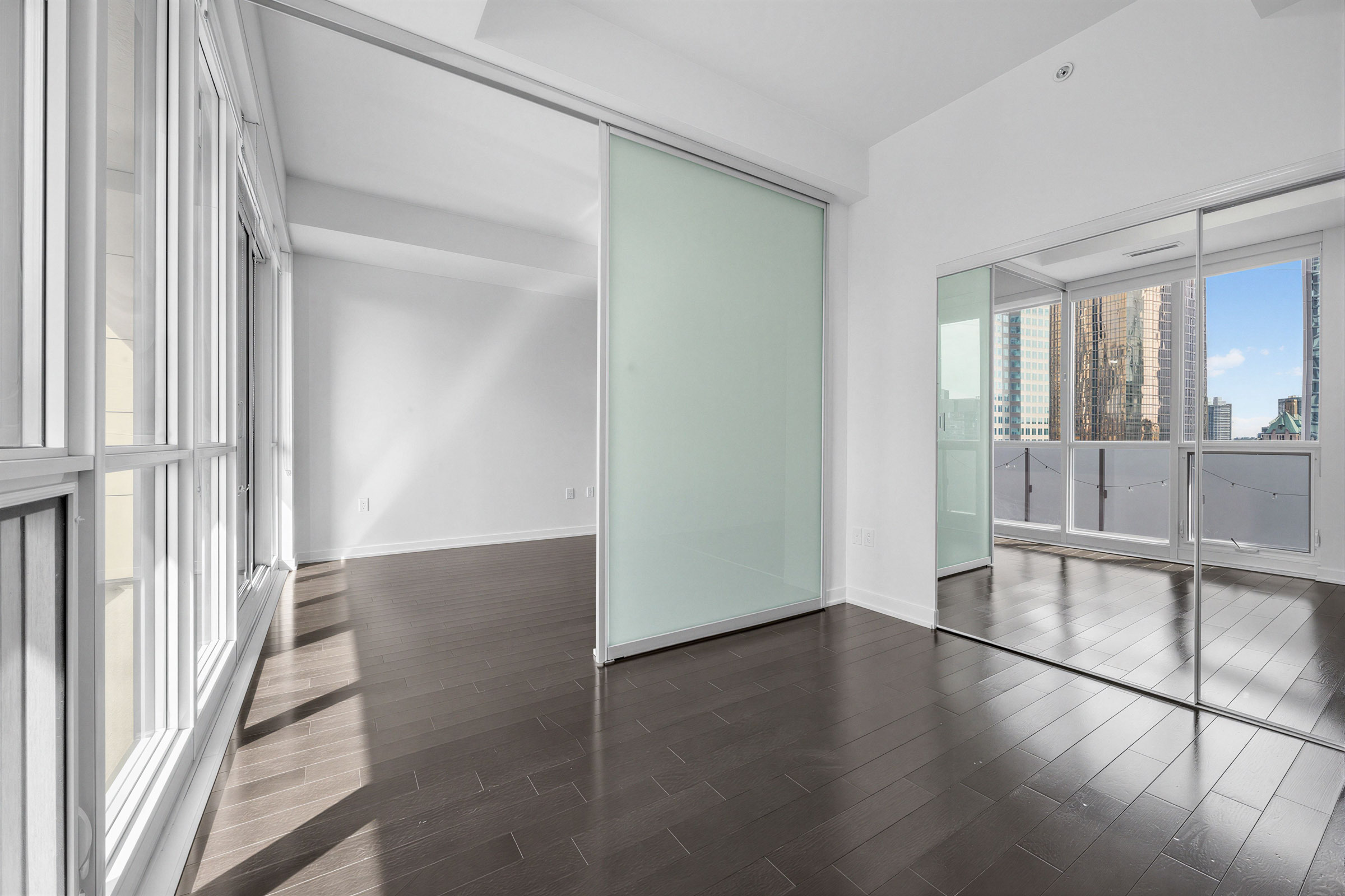 Condo bedroom with dark brown hardwood floors and large sliding door. 