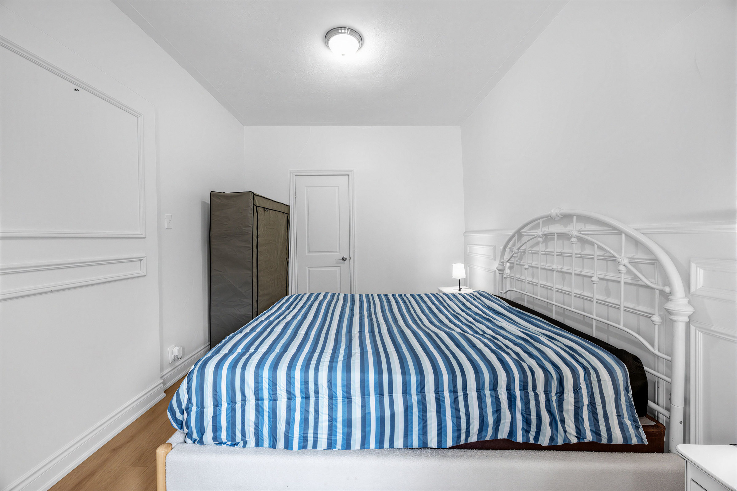Primary bedroom with bed, gray walls with wainscotting and door to second bedroom.