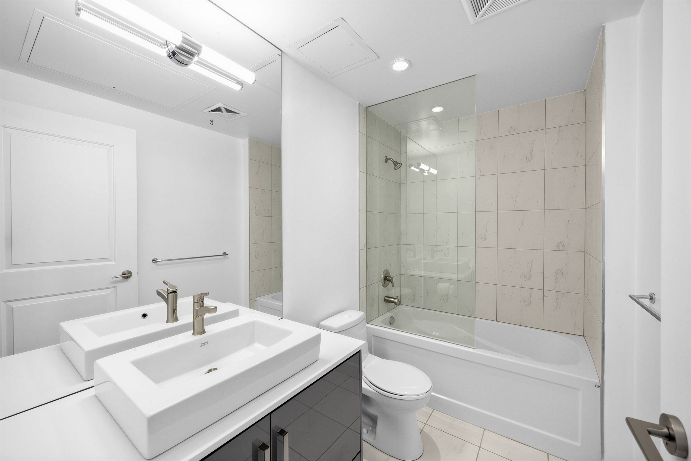 1 The Esplanade Unit 3403 4-piece bath with vessel sink, mirror-mounted light fixture, glossy cabinets, ceramic tiles, and soaker tub with glass partition.