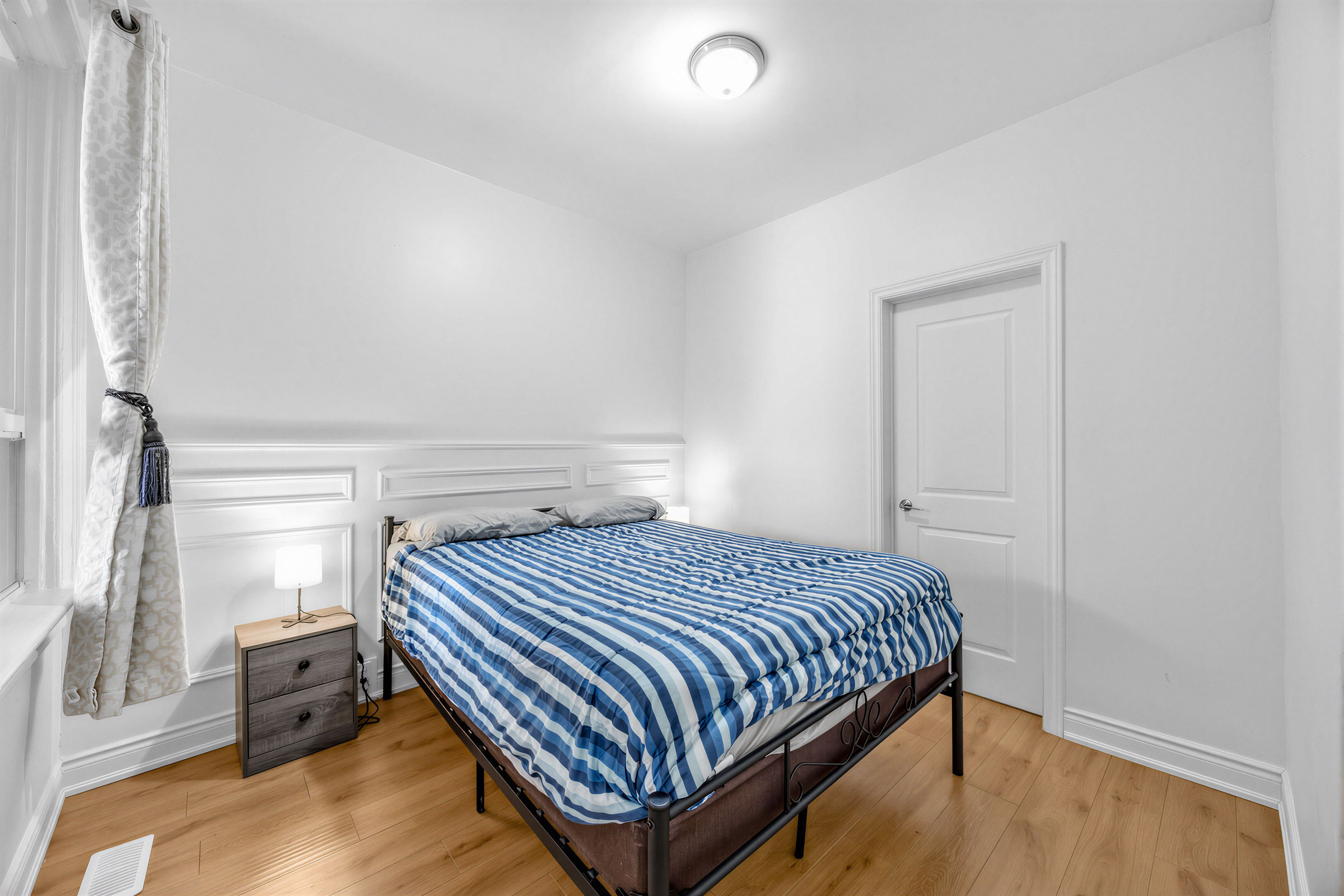 57 Shanly St 2nd bedroom with large bed, wide-plank laminate floors and white walls with wainscotting.