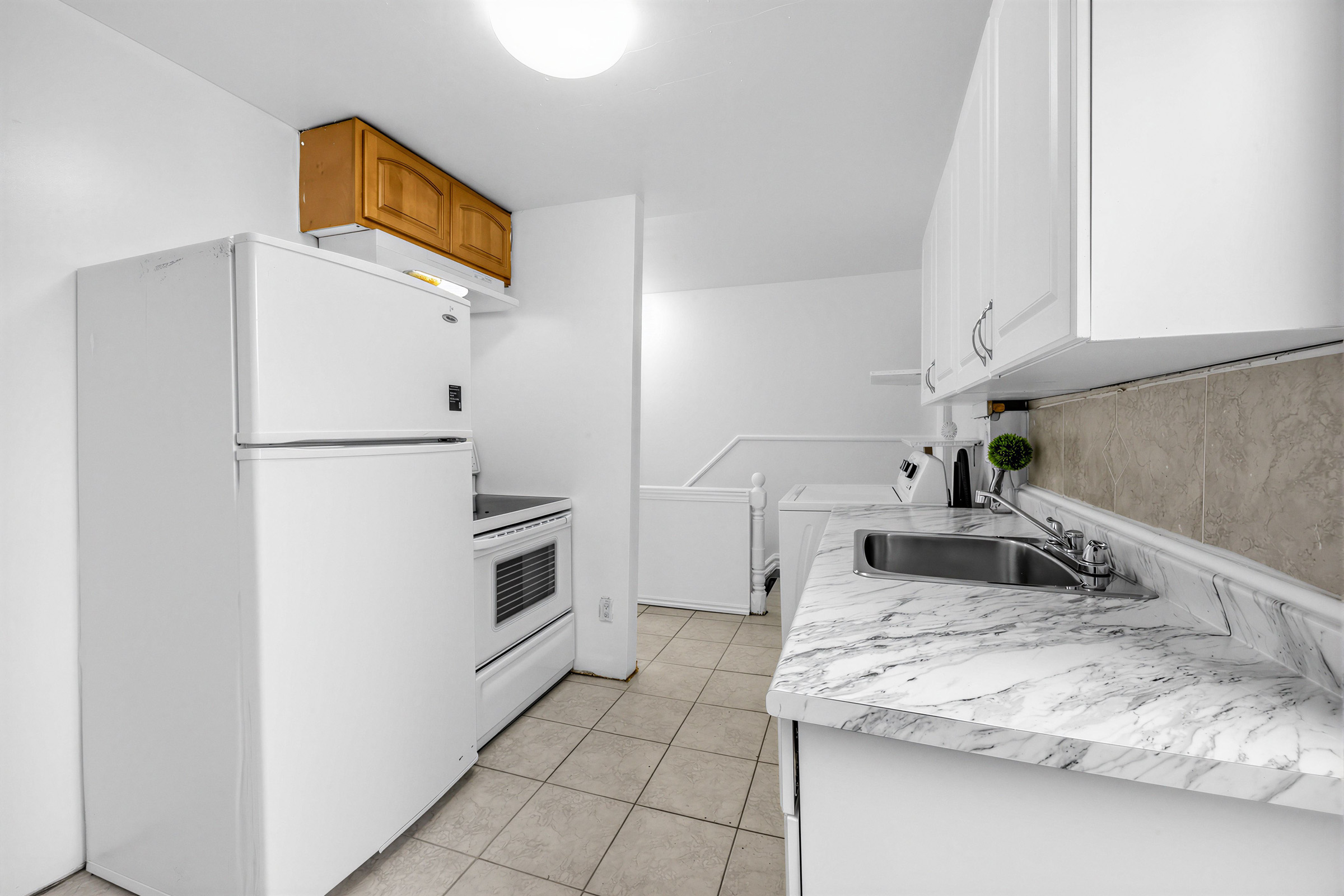 2nd floor kitchen with several cabinets, stainless-steel sink, ceramic floors and appliances.