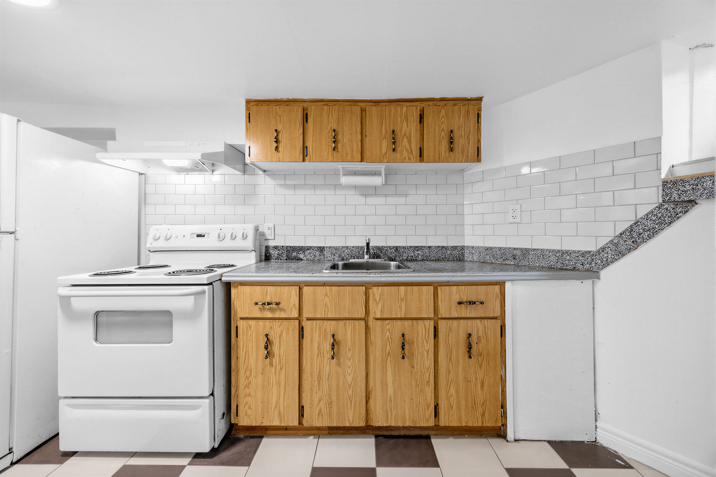 57 Shanly St basement with linear kitchen featuring dark speckled countertops, brown wooden cabinets, and a white-tiled backsplash.