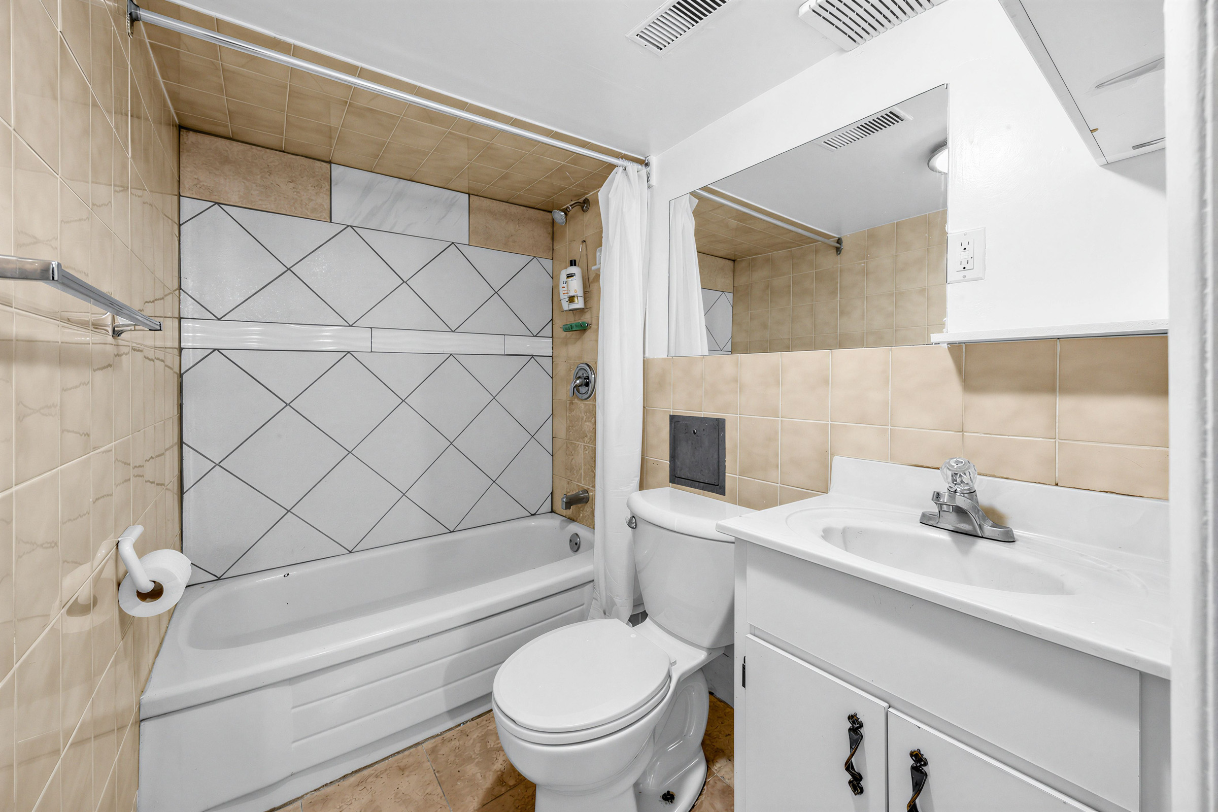 Basement bath with tub, beige tiles, sink with cabinets, and wide vanity.