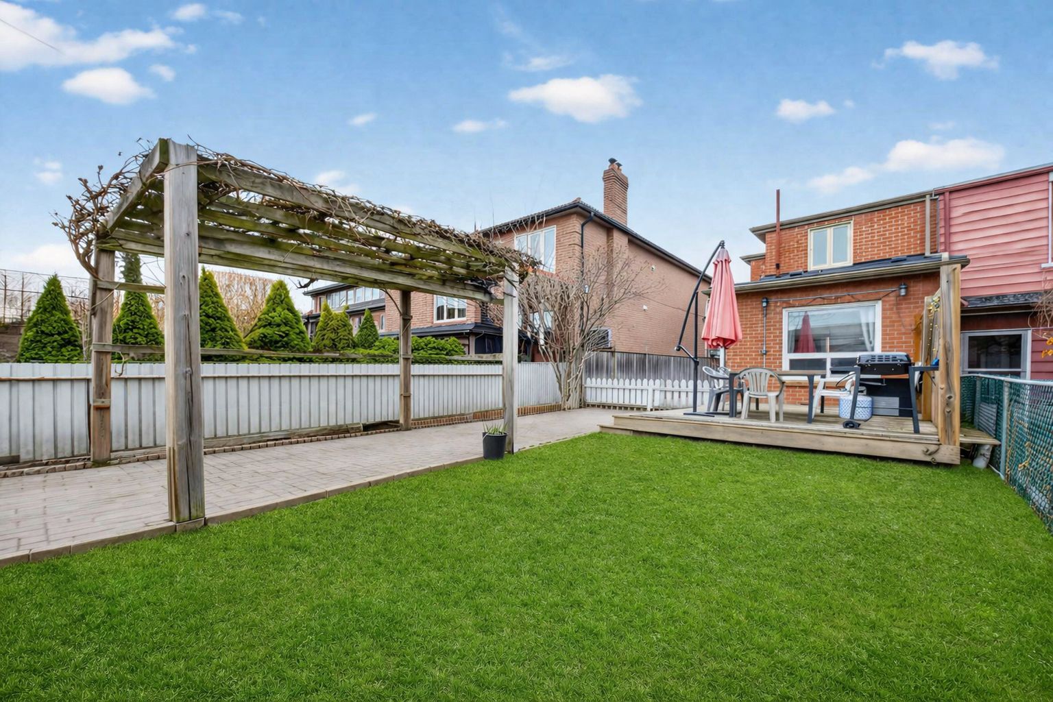 Spacious backyard lawn with pergola to left and deck near top.