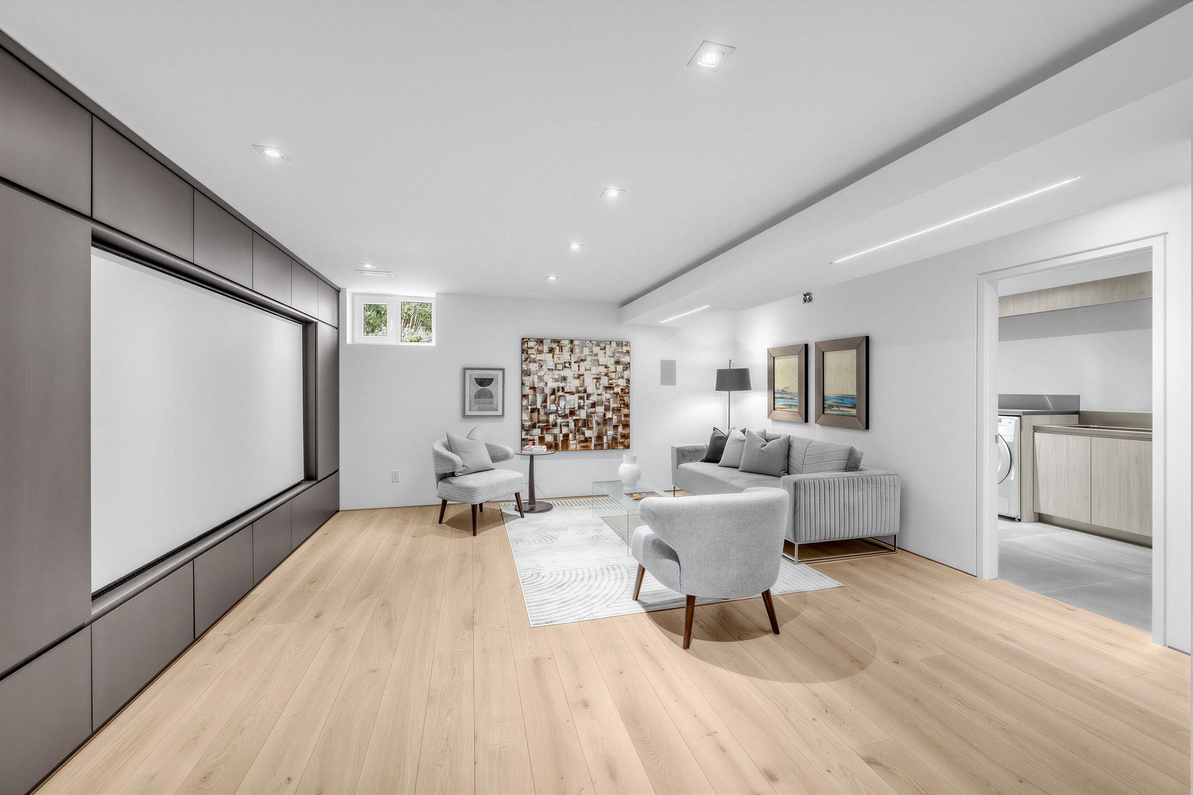 Basement media room with sofa, chairs, window, recessed lights, and large media wall with projection screen.