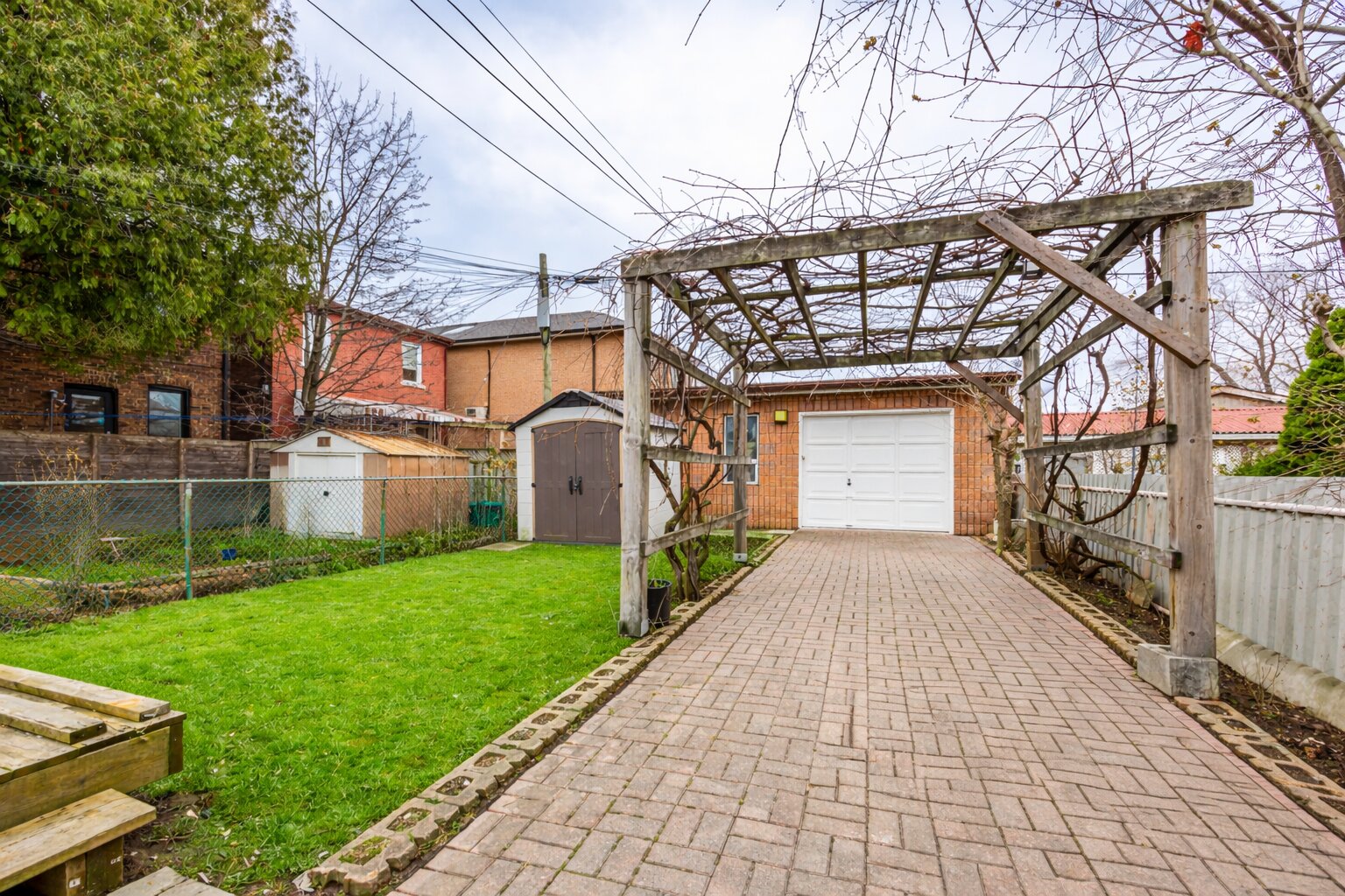 57 Shanly St's pergola with climbing plants, paved path below, and shed and garage in distance.
