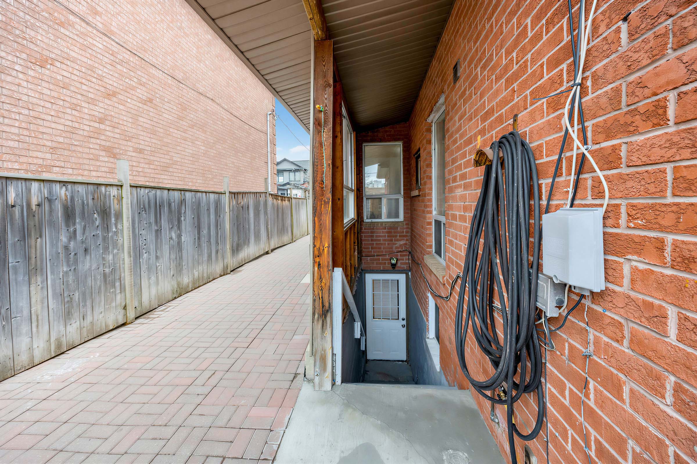 Driveway with light coloured interlocking concrete pavers and view of steps leading down to basement.