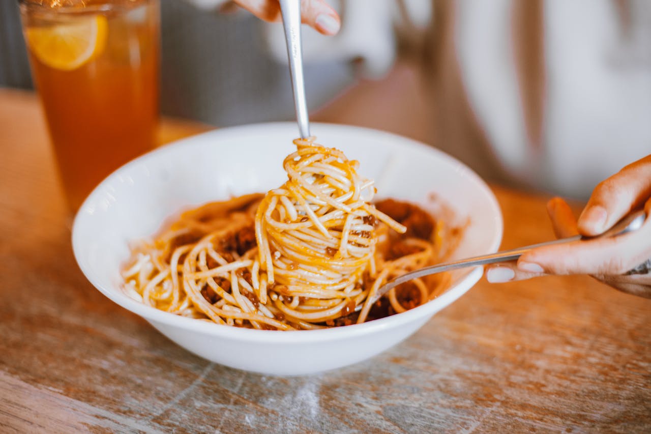 Close up of white bowl of spaghetti with strands twirled around silver fork.