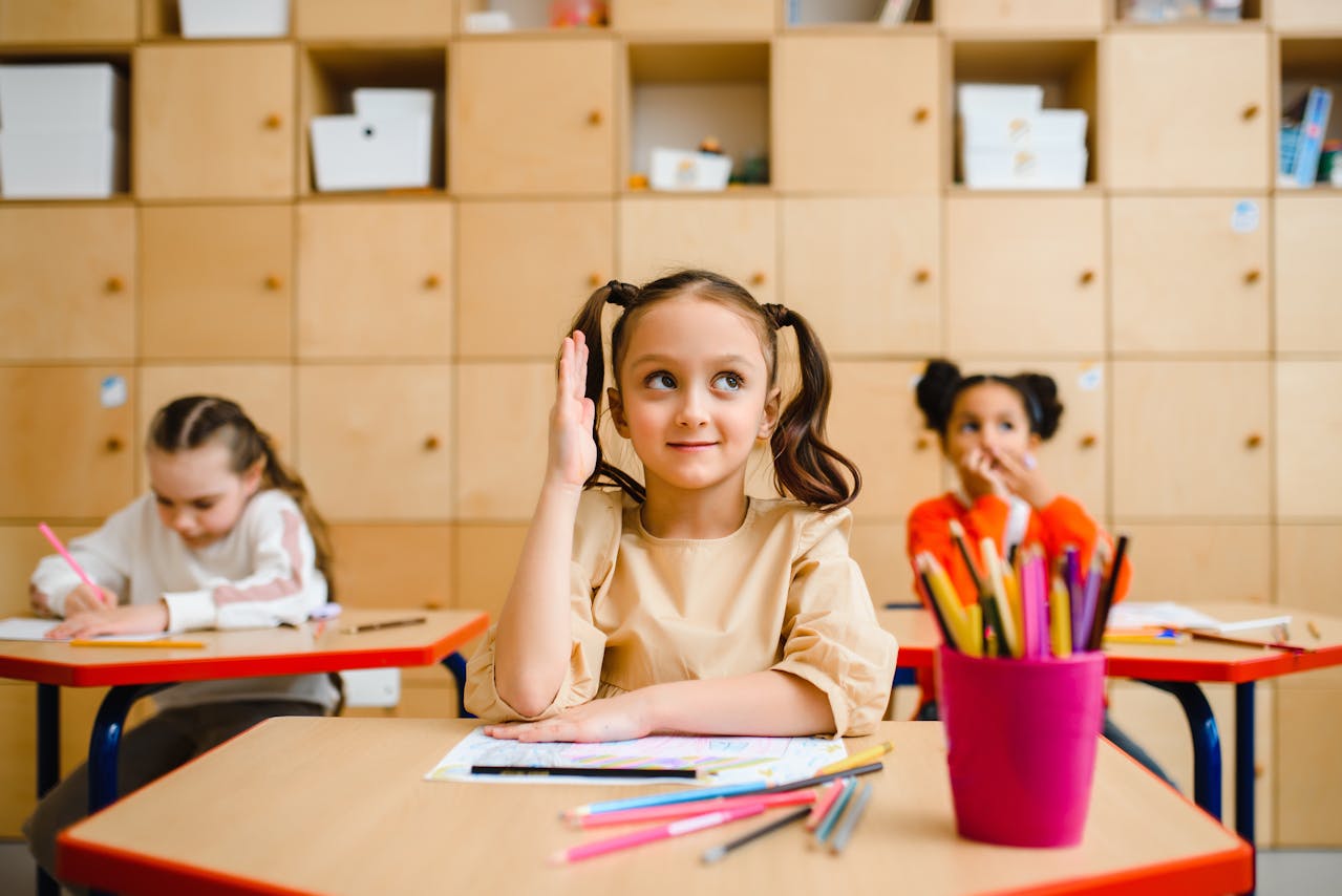 Young elementary school girl raising her hand in a classroom.