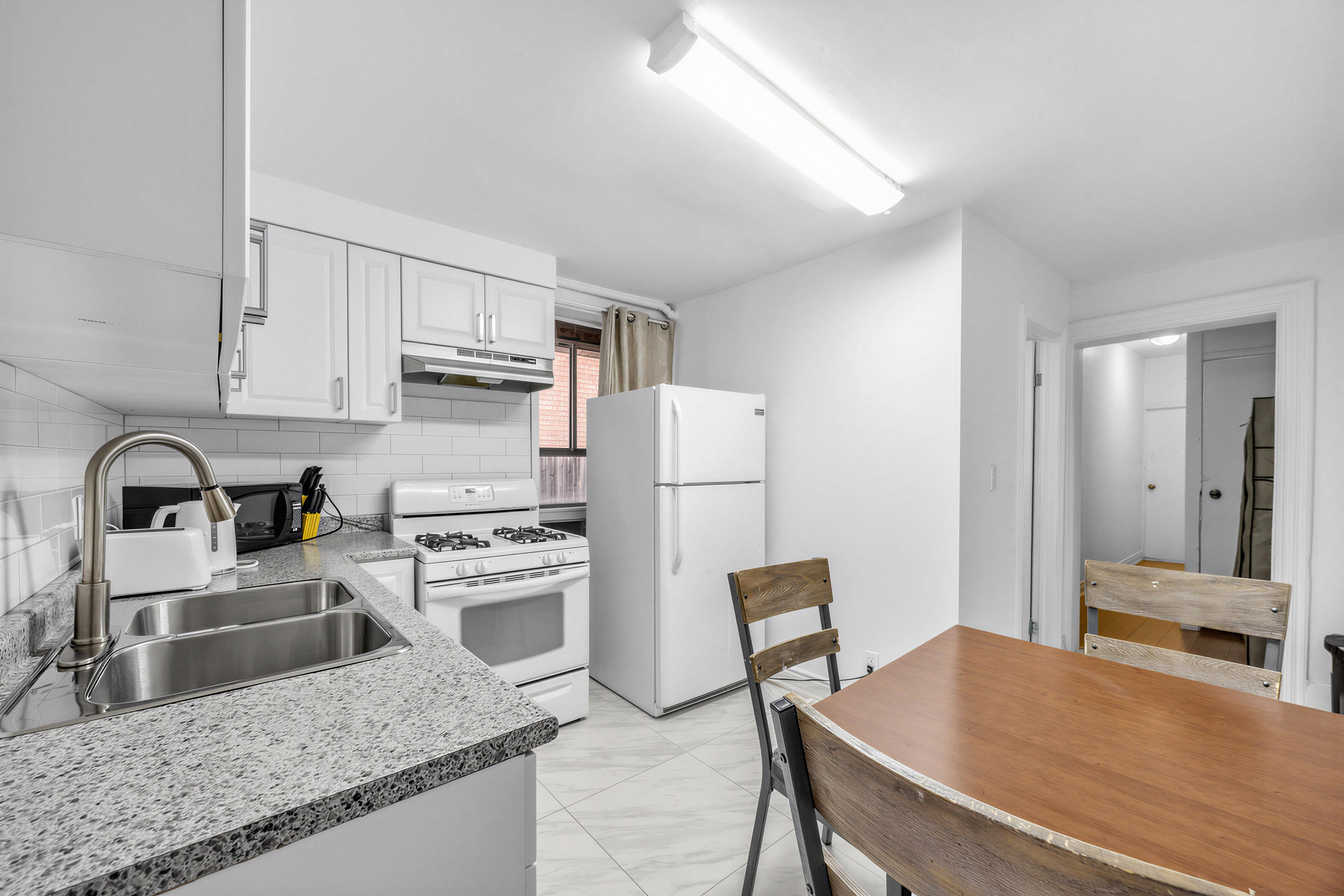 Kitchen with speckled gray counters, white storage cabinets, white tiles, white fridge and stove.