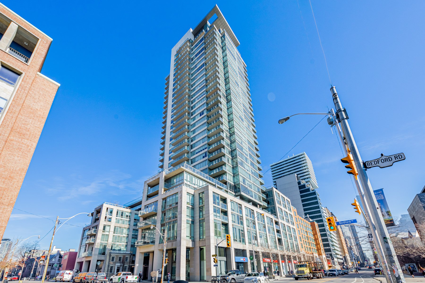 Across-the-street view of One Bedford, a modern condo with a limestone body, blue-glass windows, cantilevered balconies and overhanging roof.