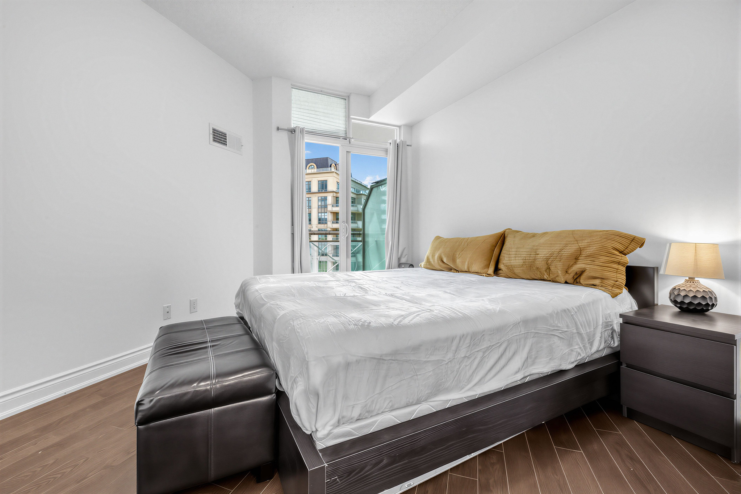 Condo bedroom with bed and walk-out balcony with view of building in distance.