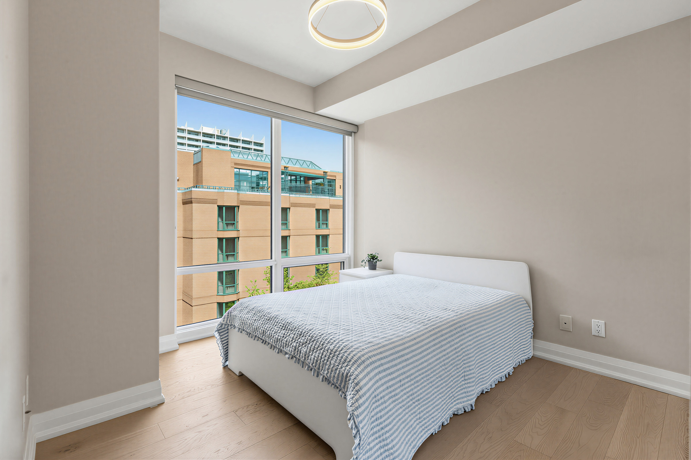 1 Bedford Rd Unit 603 primary bedroom with large bed and tall windows overlooking amenity garden.