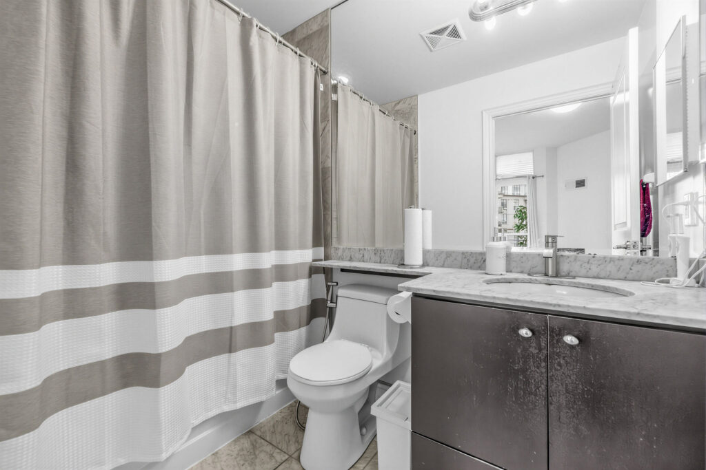 20 Bloorview Place Unit 1003's primary bath with wide vanity, mirror-mounted lights, sink with brown cabinets and soaker tub with curtain.