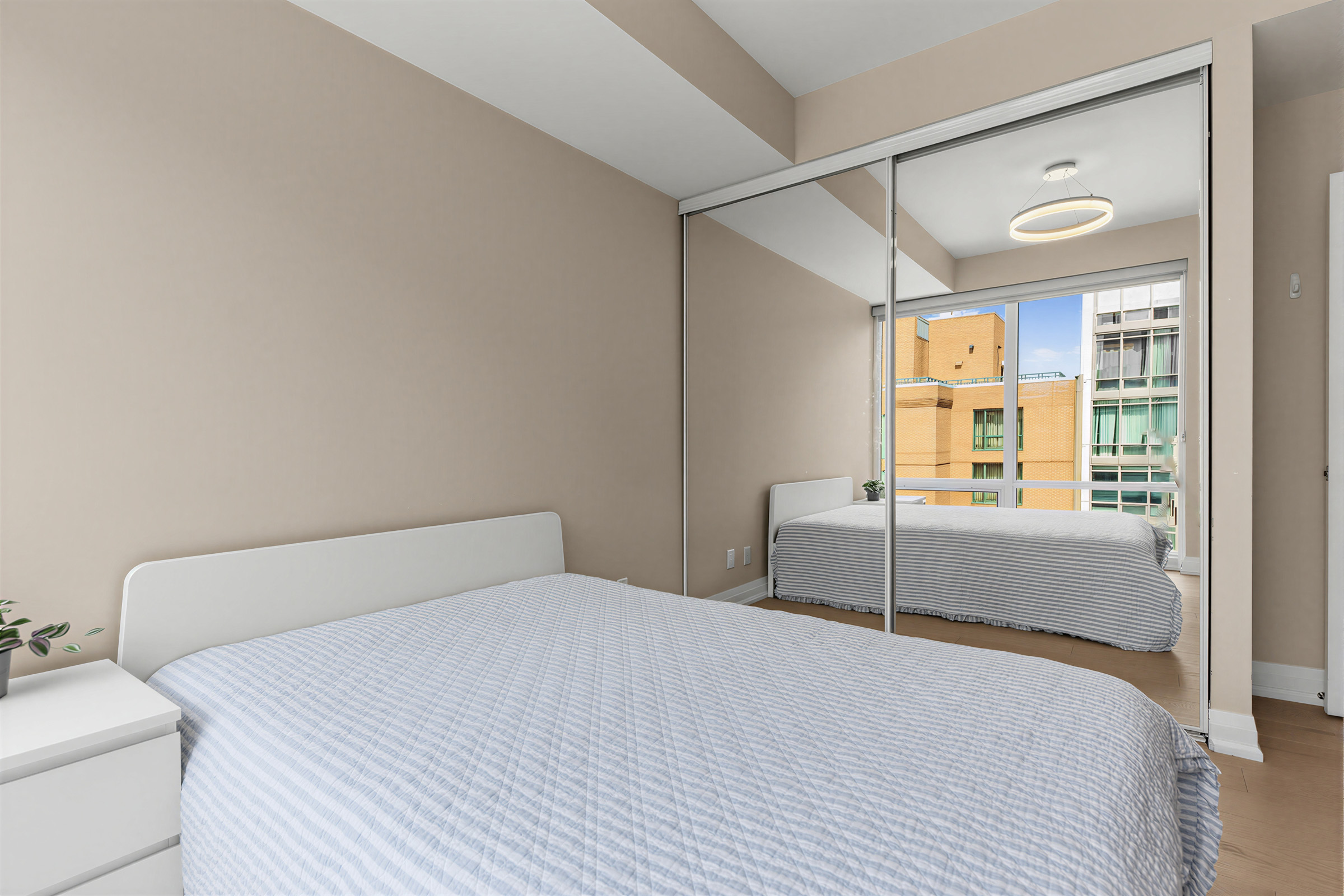 Bedroom with large bed, beige walls, warm hardwood floors, and large mirror-door closet.