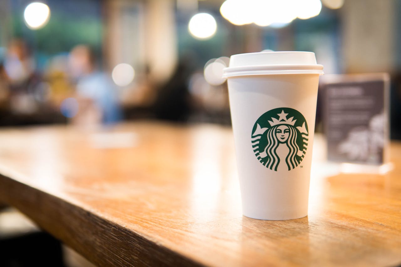 White Starbucks cup on table in foreground, customers in background.