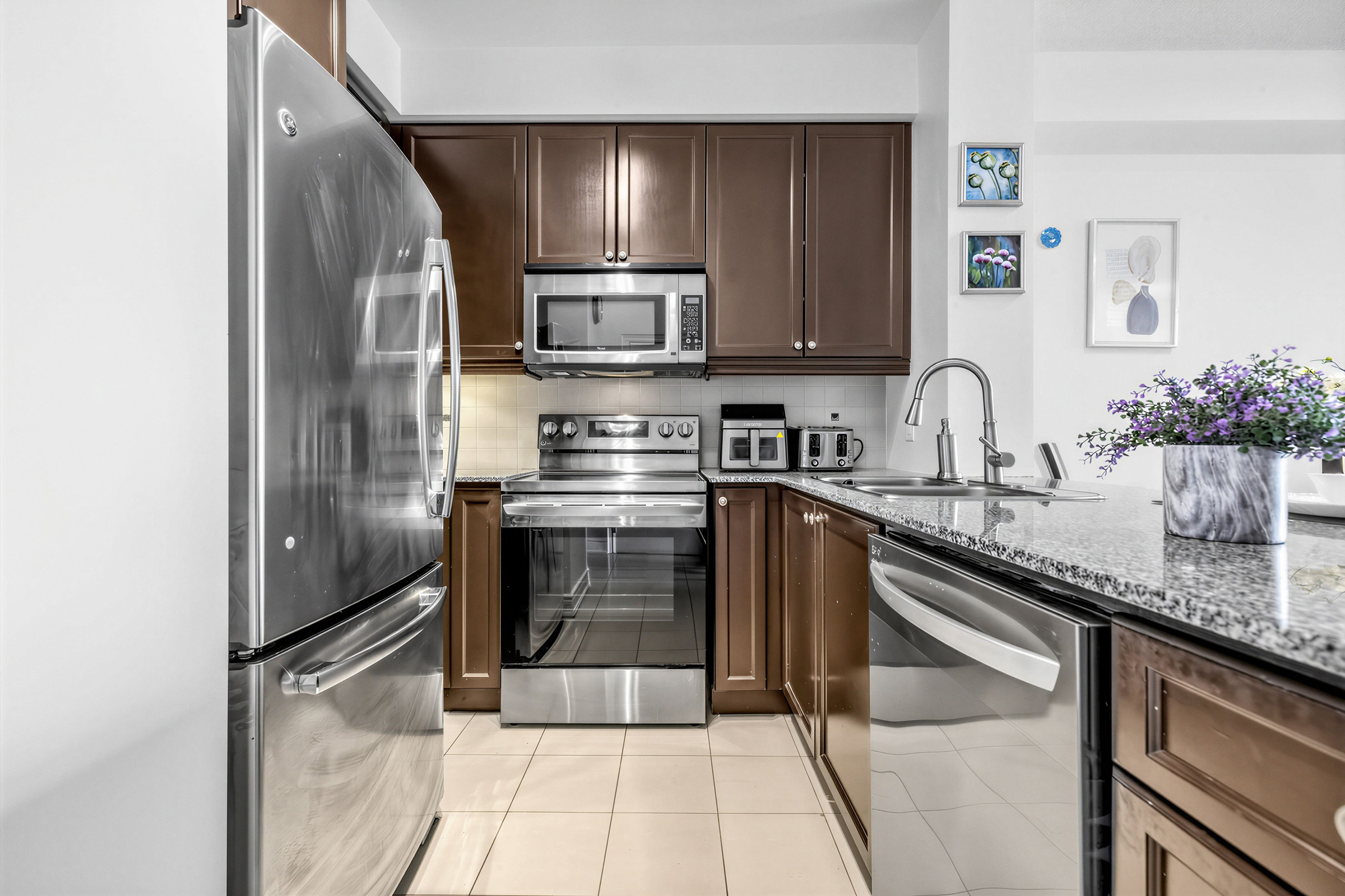 20 Bloorview Place Unit 1003 kitchen with dark brown cabinets, beige tiles and stainless-steel appliances.