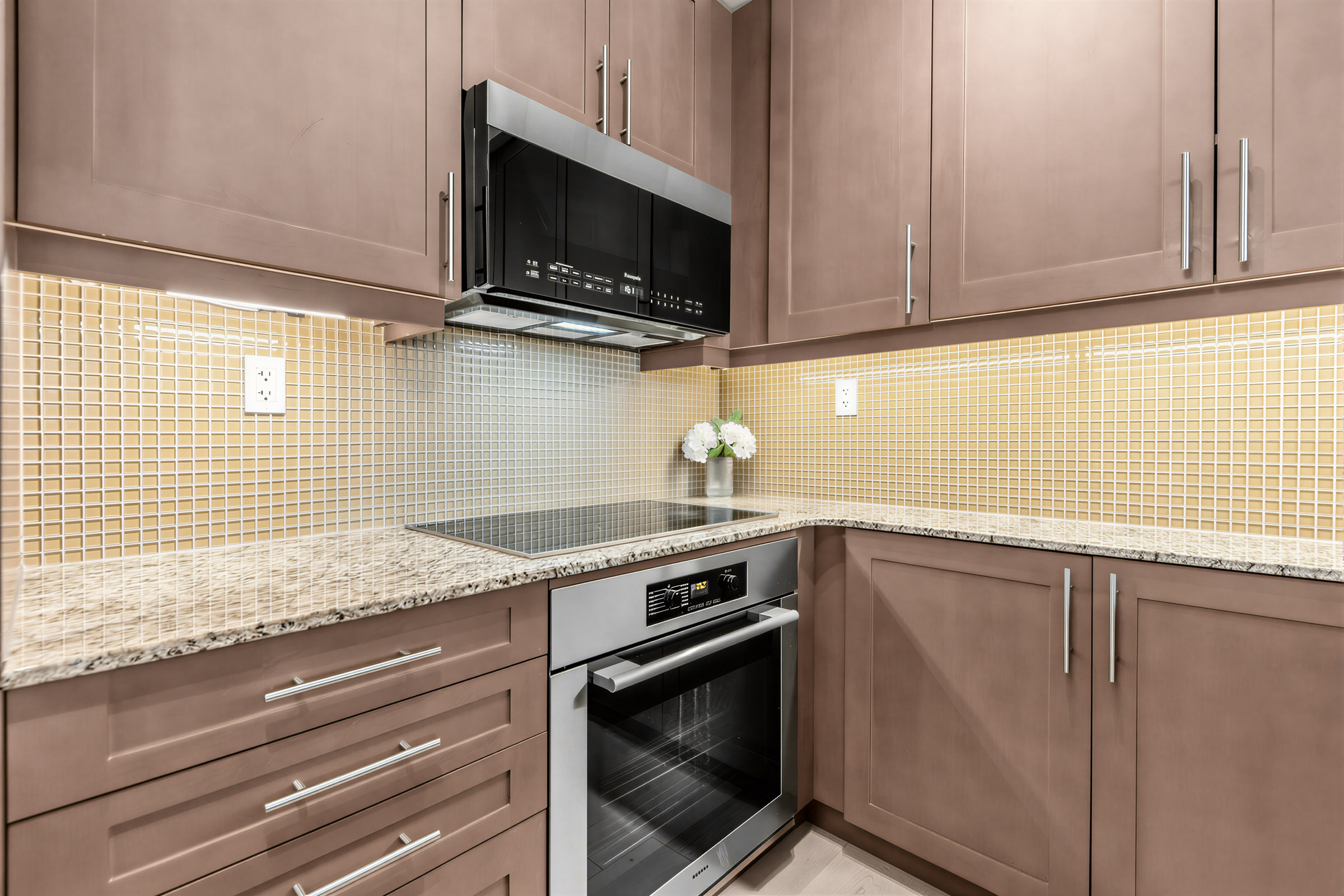 Condo kitchen with mosaic backsplash with earth-toned cabinets.