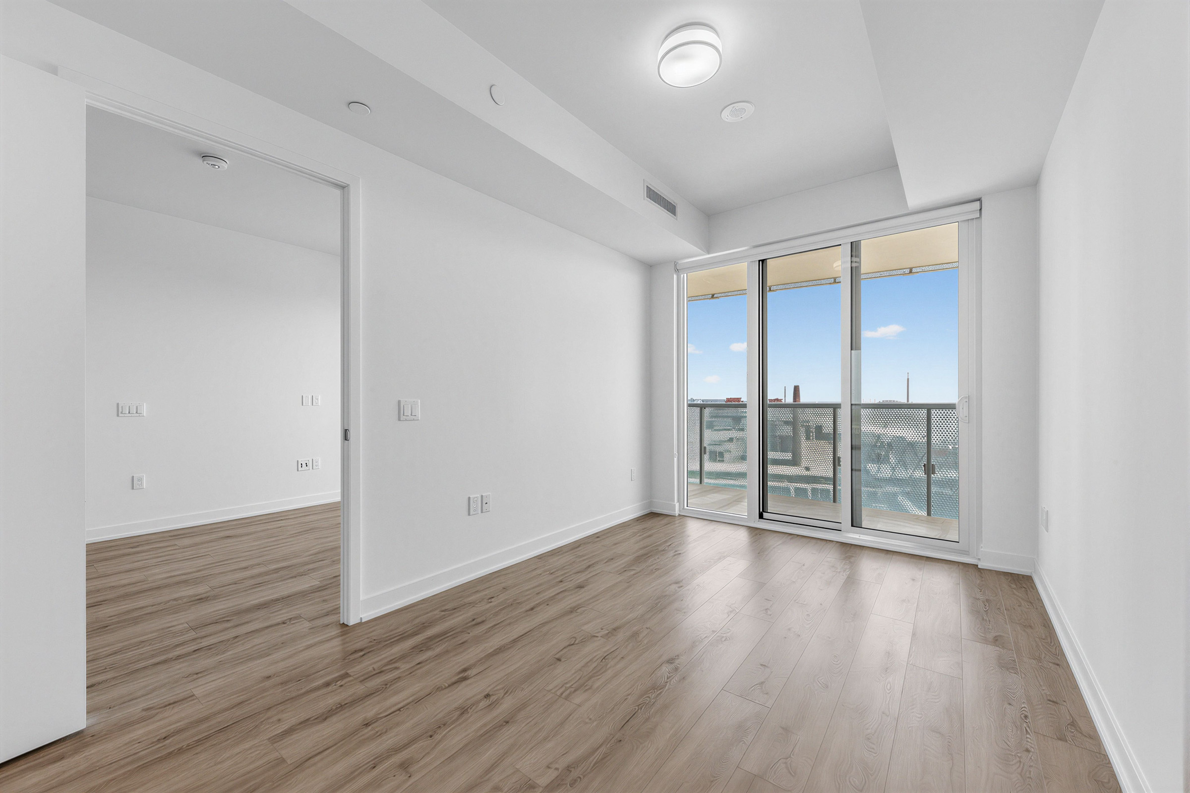 Condo bedroom with hardwood floors and circular ceiling lamp.