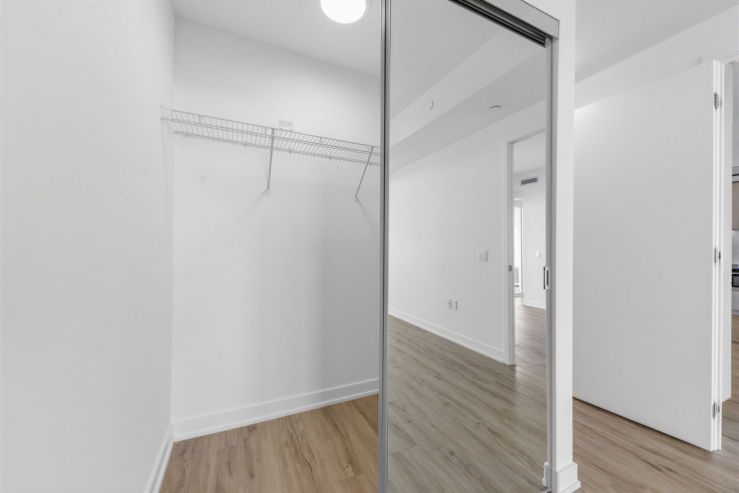 Double door condo closet with built-in racks, ceiling light and mirror doors.