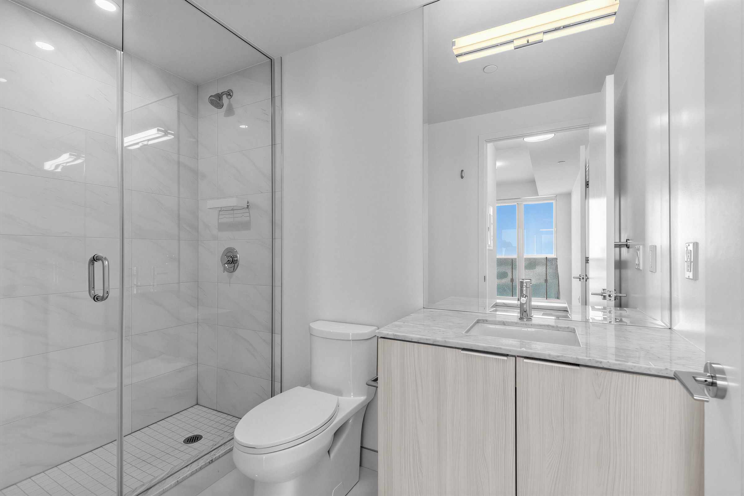 15 Queens Quay E Unit 1901 primary ensuite bath with frameless glass walk-in shower, white porcelain tiles, and tall vanity with mirror-mounted lights.