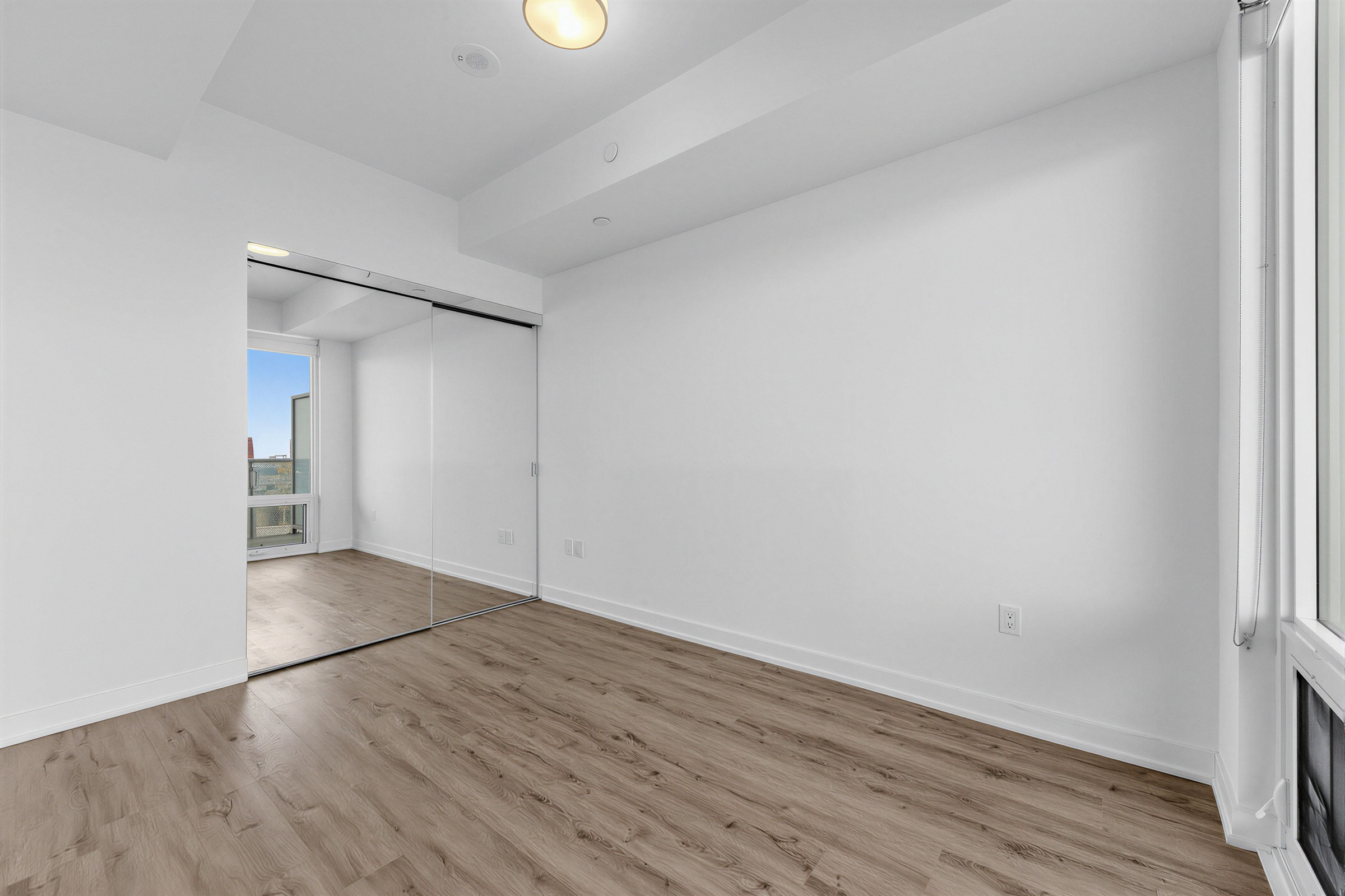 Empty condo bedroom with large mirror-door closet.