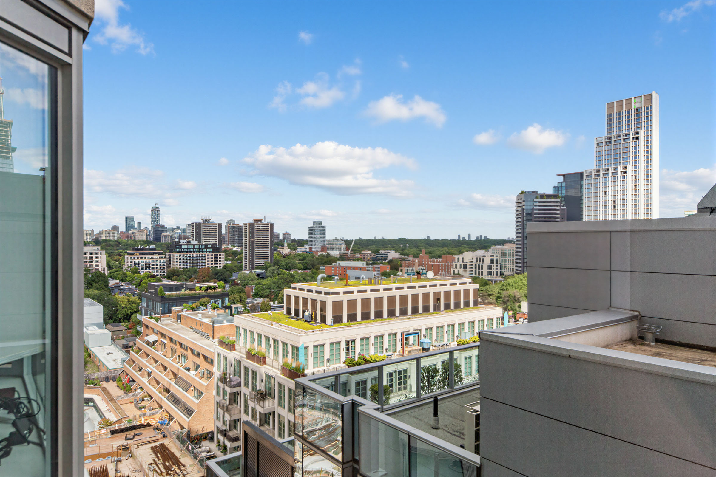 View of building tops, trees, greenery and blue skies from condo bedroom window.