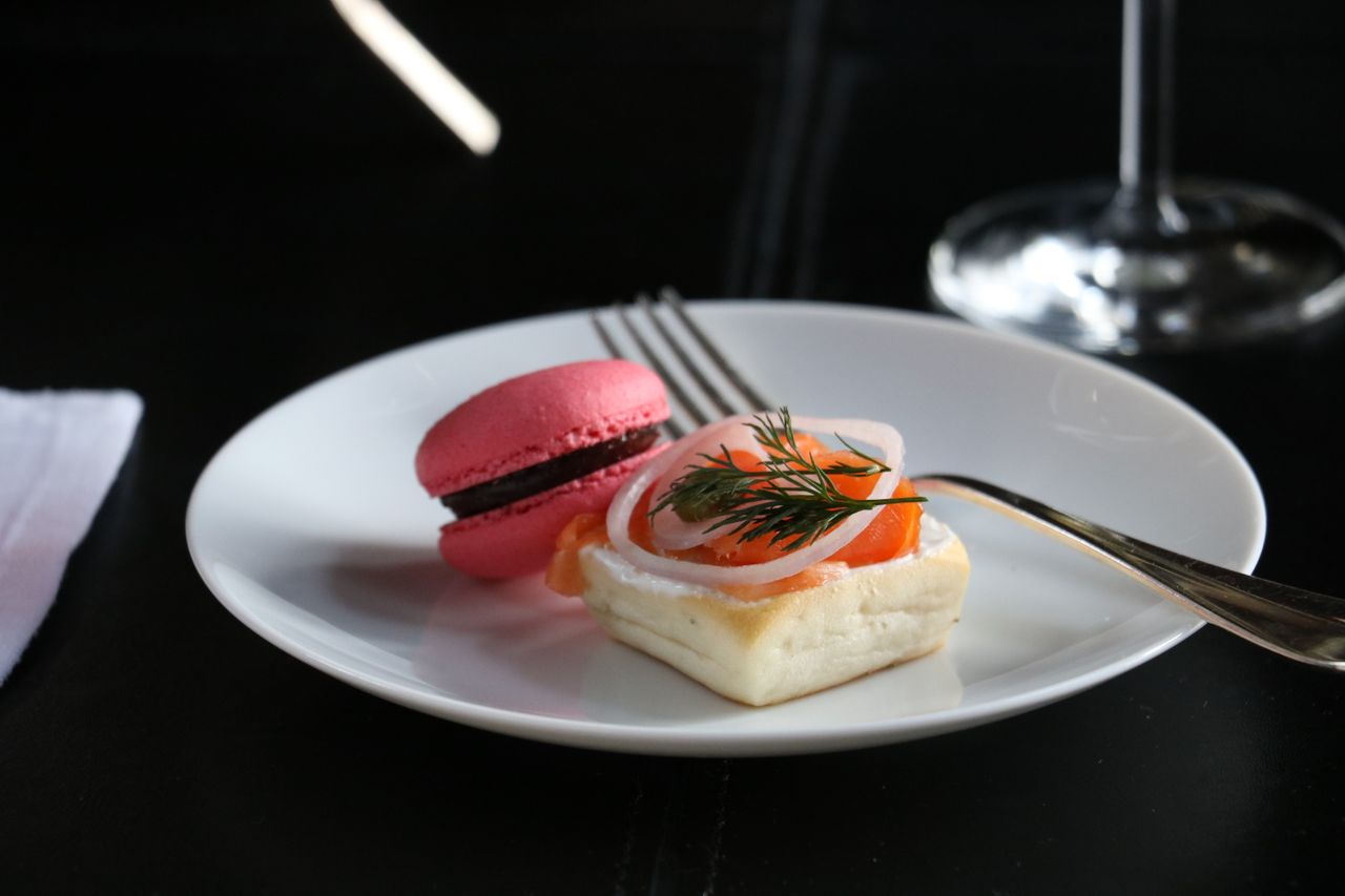 Close up of white ceramic plate with pink macaron and dessert.