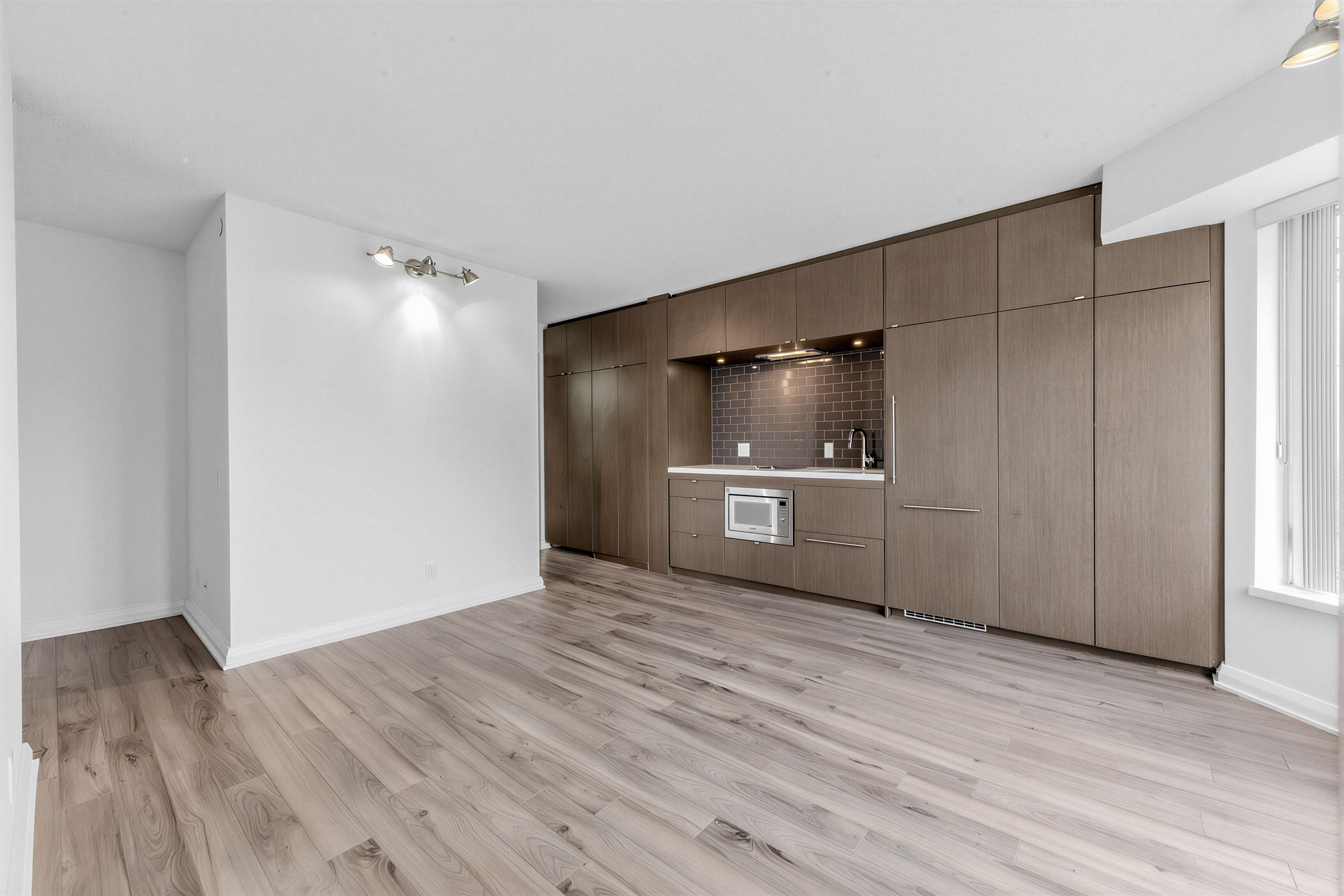 Condo living and dining rooms with dark laminate floors and wall-mounted lights.